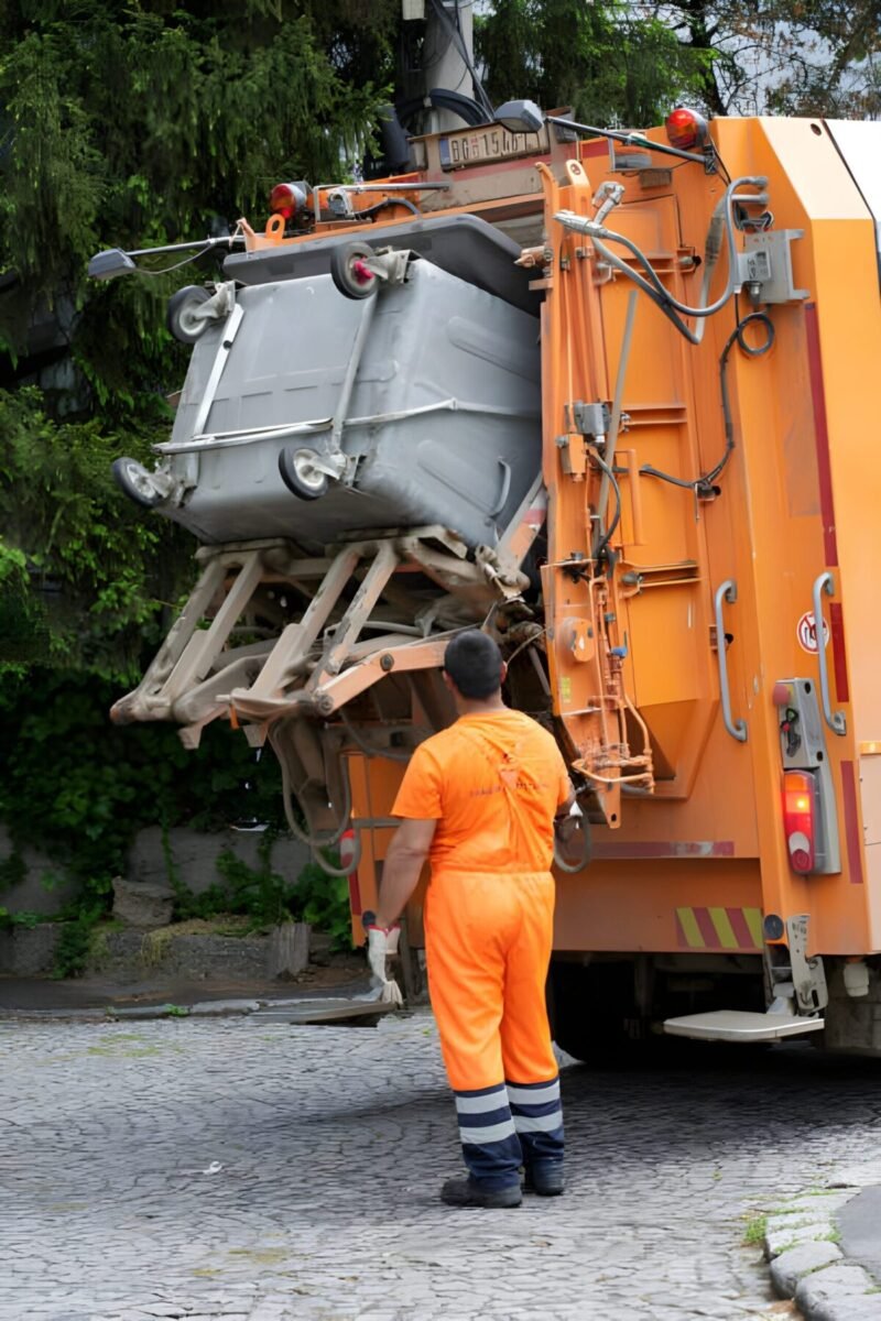 Worker loading trash bin into garbage truck