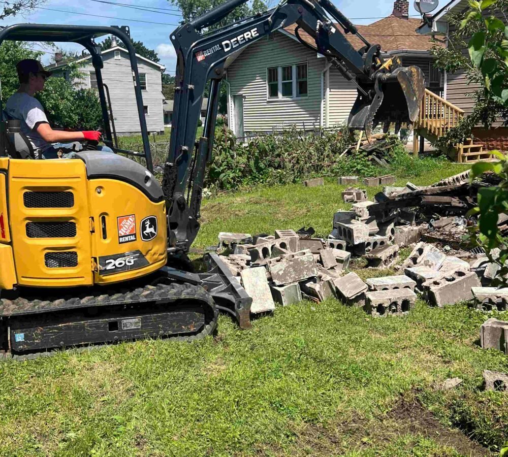 A man is operating a yellow excavator in a yard.