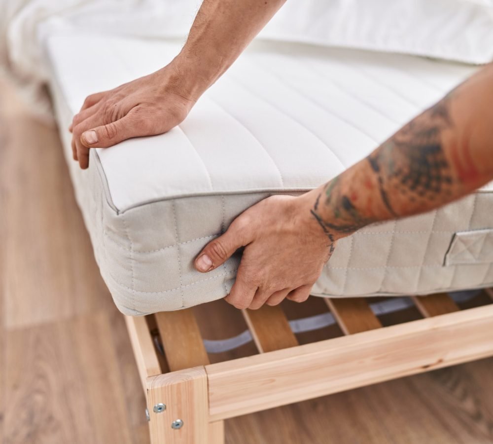Young man holding mattress at bedroom